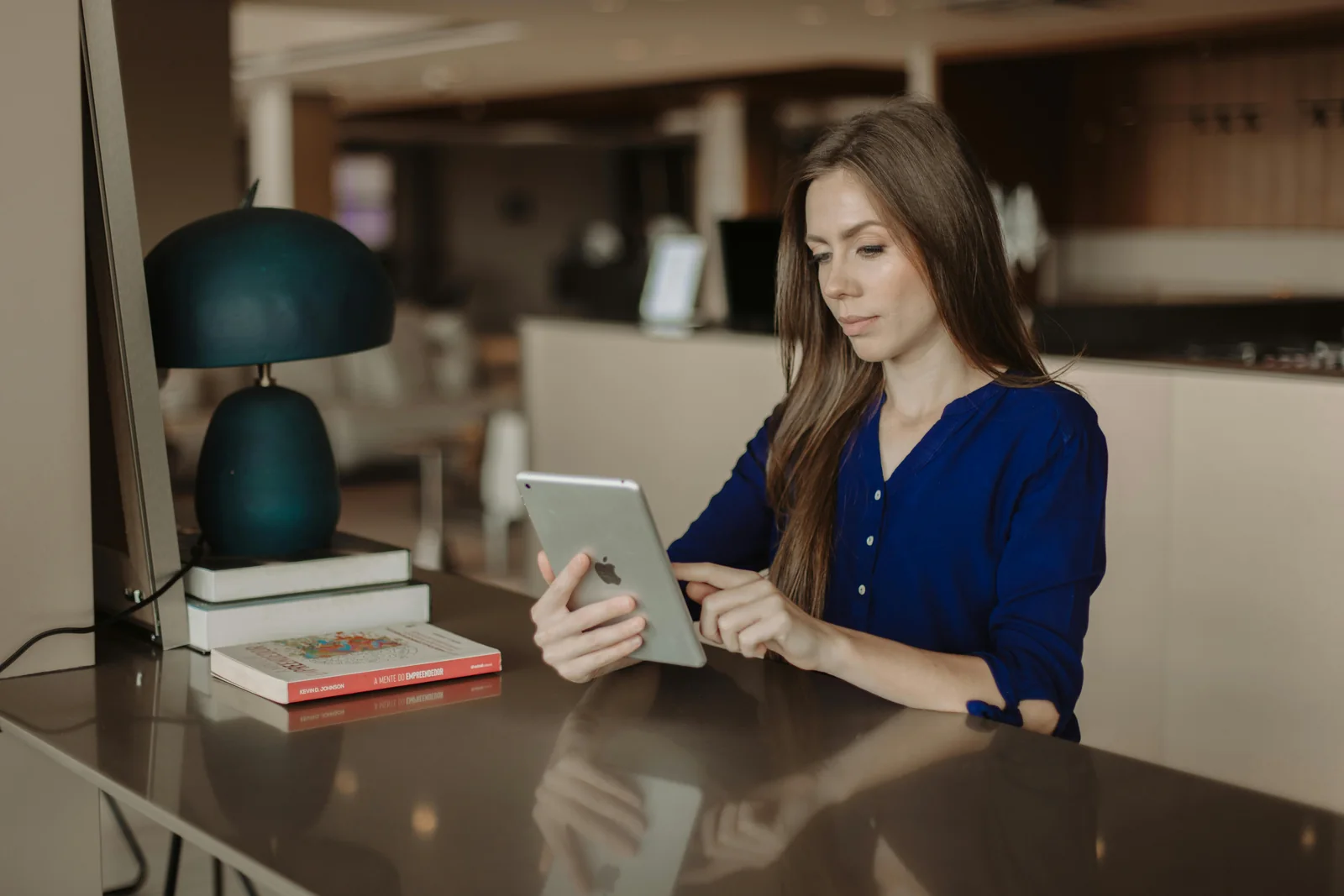 Mujer utilizando una tableta junto a una lámpara y unos libros