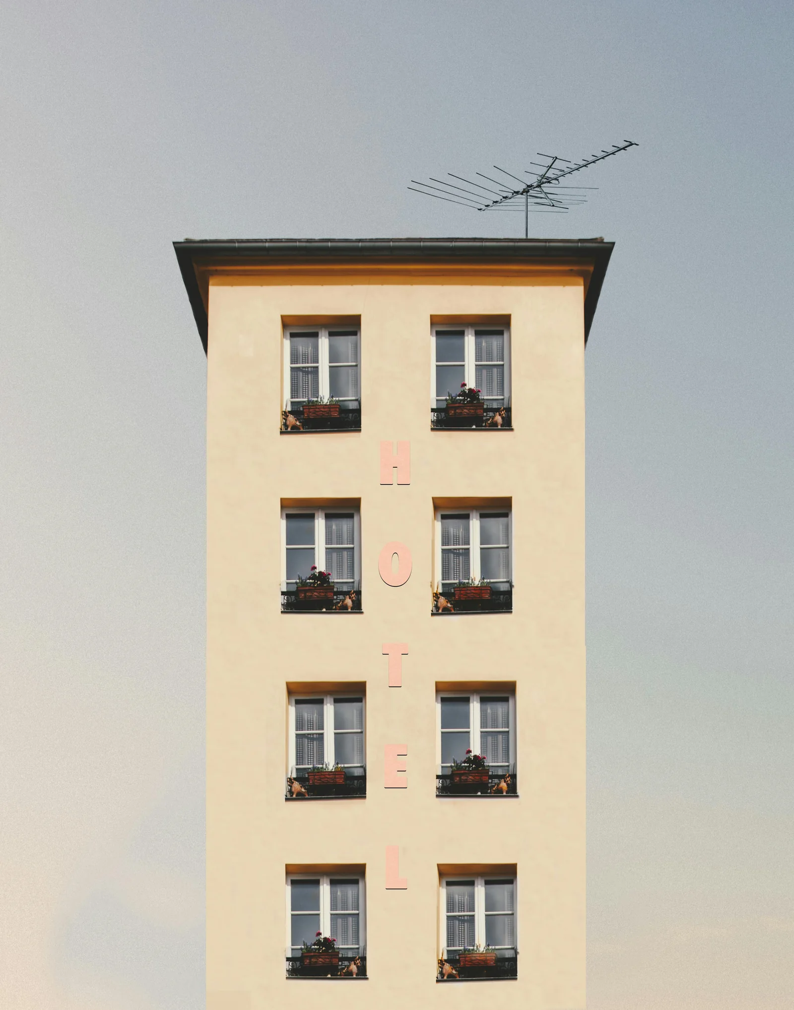 A hotel's yellow facade with windows, flower boxes and a vertical sign