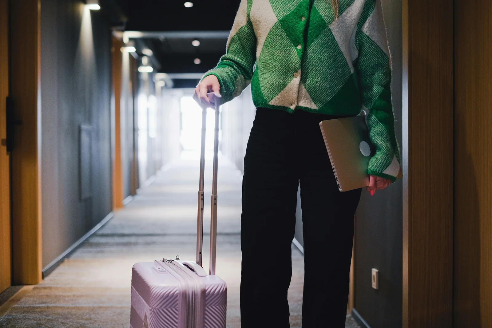 Huésped con una maleta de ruedas y un portátil en el pasillo de un hotel