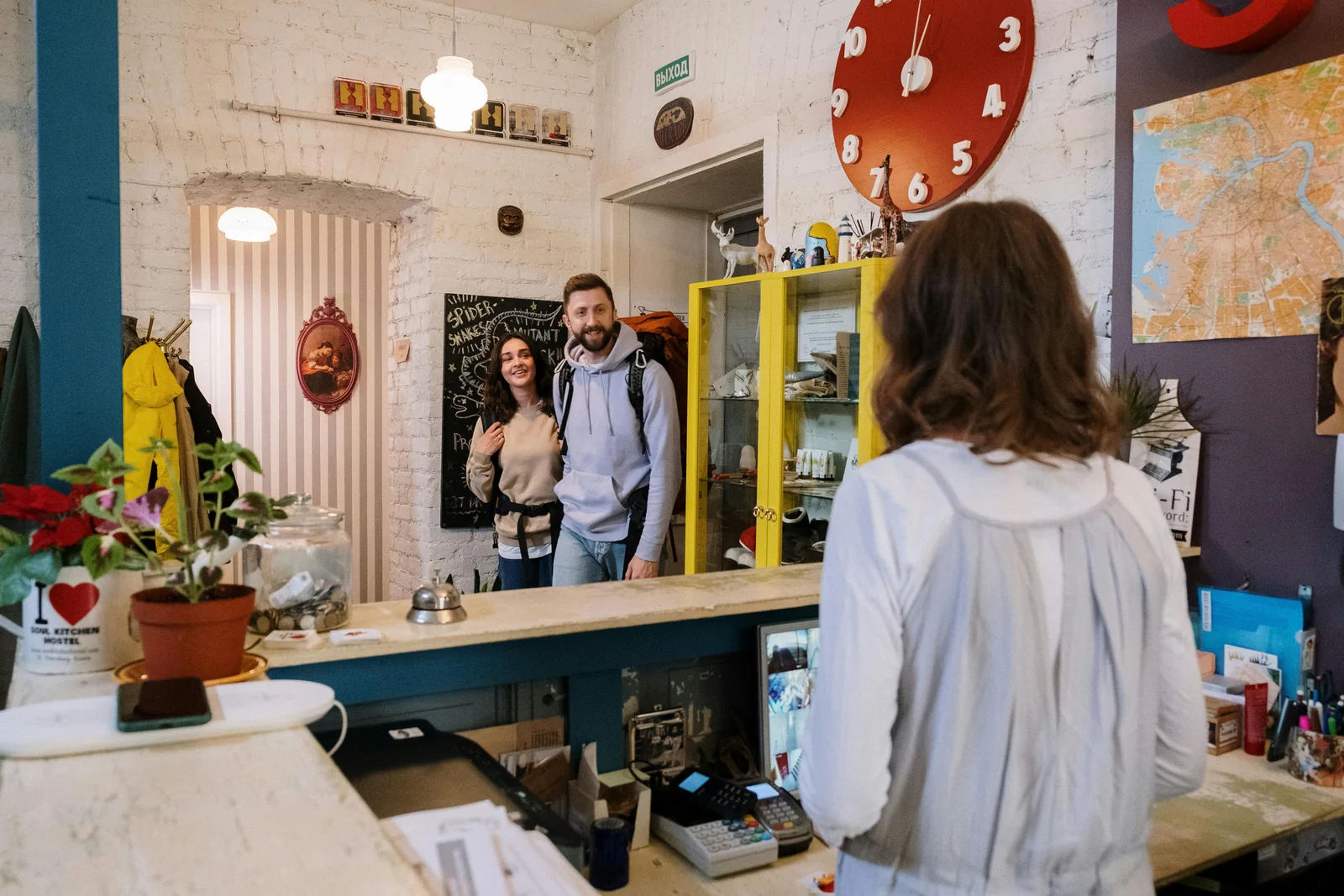 Dos viajeros con mochilas son recibidos en el mostrador de un alojamiento