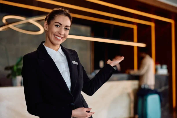 A smiling receptionist beside a counter gesturing toward the reception area