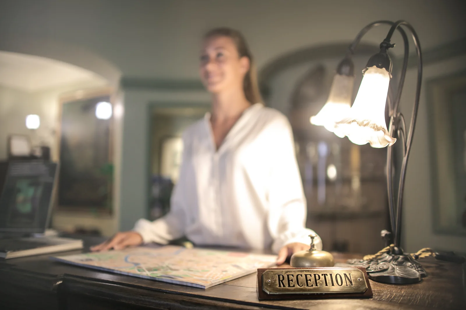 A reception counter with a map, a bell and a lamp, with a receptionist in the background