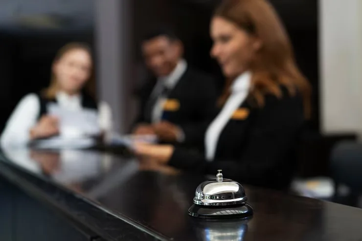 Timbre plateado en primer plano sobre un mostrador de recepción, con personas desenfocadas al fondo
